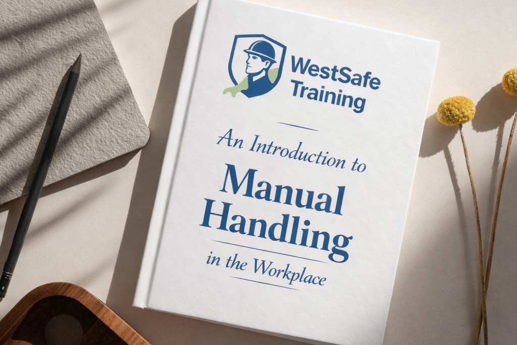 WestSafe Training manual handling training book titled “An Introduction to Manual Handling in the Workplace” displayed on a neutral desk with notebook, pencil, wooden tray, and yellow flowers, professional workplace safety training course cover.